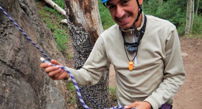 A person wearing safety gear smiles as they hold a rope. 